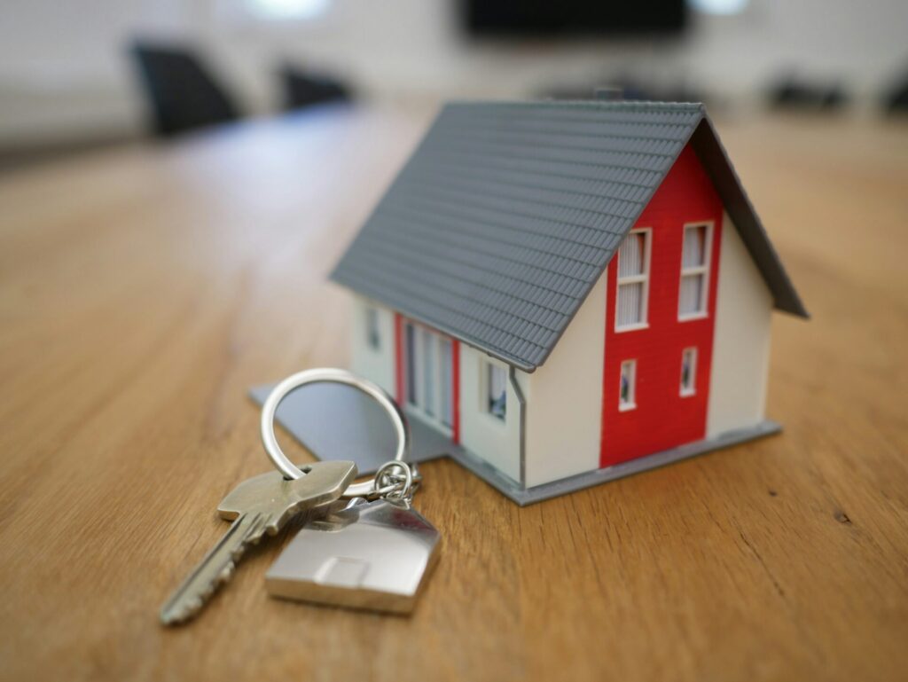 A close-up of a small model house, representing the Airbnb business model, with a red and white exterior and a keyring, symbolizing real estate and property investment.