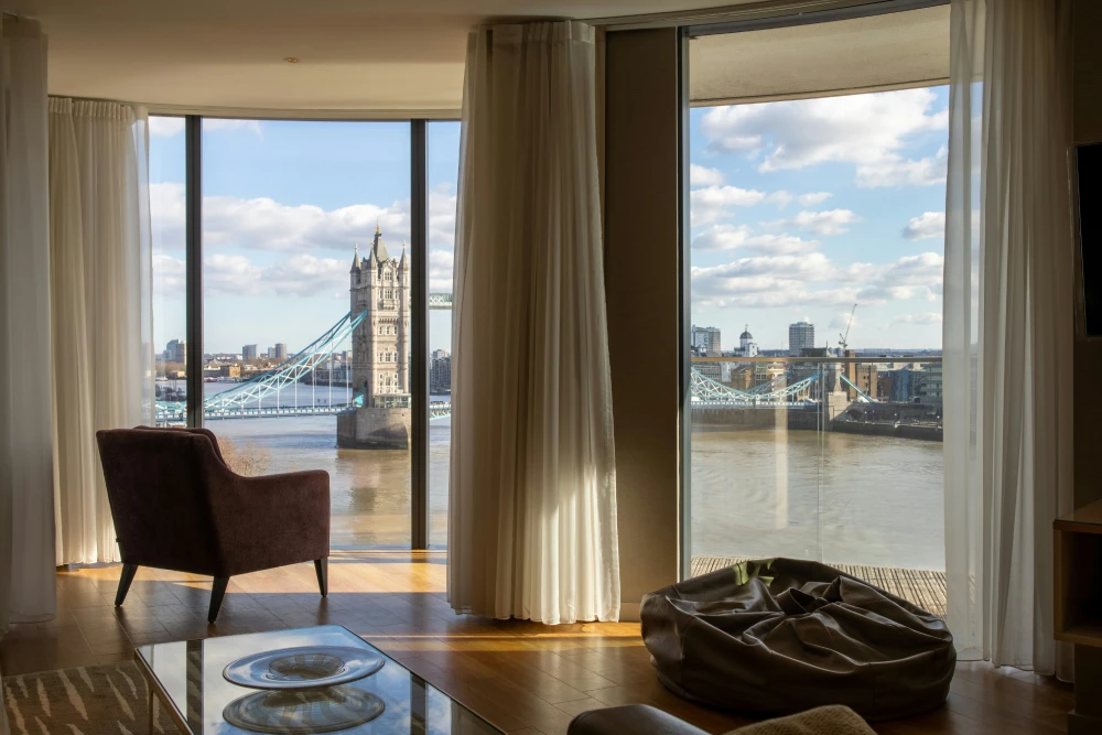 Modern London serviced apartment living room with floor-to-ceiling windows overlooking Tower Bridge and the River Thames, showcasing serviced accommodation management London.