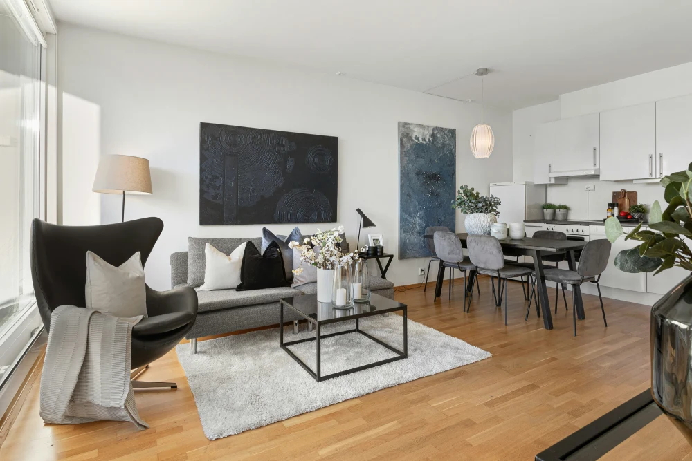 Bright open-plan living room and kitchen with grey sofa, black armchair, dining table and contemporary artwork, illustrating a well-presented Airbnb rental in the UK.